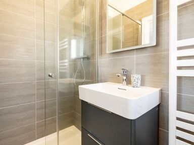 A bathroom with a shower enclosure, a white sink with a dark cabinet, a wall-mounted faucet, a mirror, and a white towel radiator at Artemis Rock
