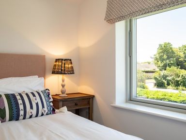 A bedroom with a bed white bedding a striped pillow a wooden nightstand with a lamp and a window showing green trees at Artemis in Rock