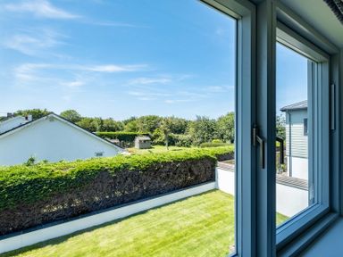 A view of a garden with a hedge and houses beyond seen through a window at Artemis in Rock