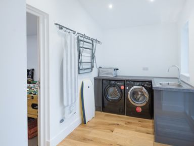 A laundry room with black washing machine and dryer a sink ironing board and wooden floor at Artemis in Rock