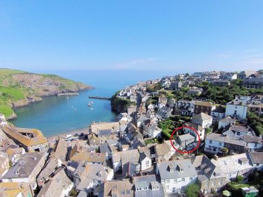 A coastal village with houses on a hillside and a bay with boats at Kipper Cottage in Port Isaac
