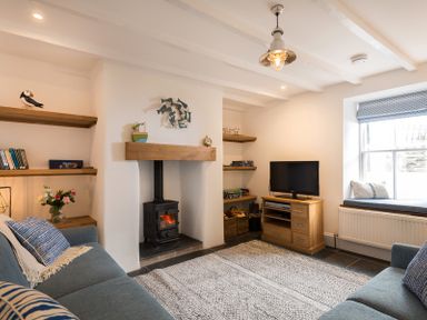A living room with a wood stove fireplace two blue sofas wooden shelves and a TV on a cabinet at Kipper Cottage in Port Isaac