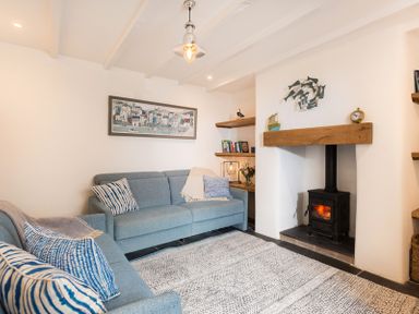 A living room with two blue sofas a wood burning stove and shelves with books and decorations at Kipper Cottage in Port Isaac