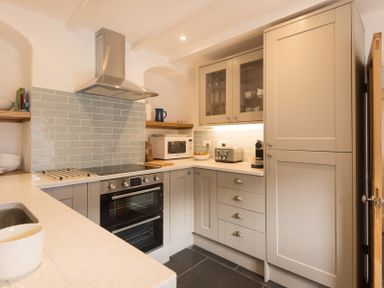 A kitchen with a stove oven microwave toaster and cabinets at Kipper Cottage in Port Isaac