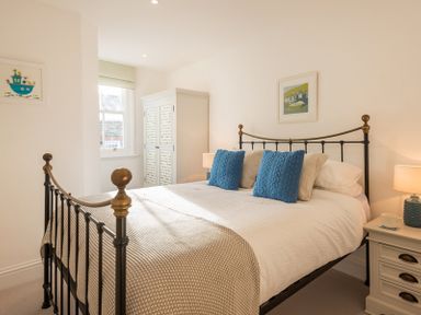 A bedroom with a metal bed frame two blue pillows a wardrobe and a bedside table with a lamp at Kipper Cottage in Port Isaac