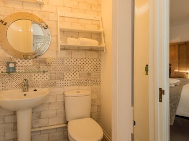 A bathroom with a pedestal sink toilet round mirror and shelves with towels at Kipper Cottage in Port Isaac