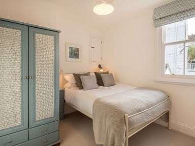 A bedroom with a bed pillows and a blue wardrobe next to a window at Kipper Cottage in Port Isaac
