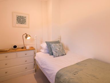 A bedroom with a single bed a green blanket a bedside cabinet with a lamp and a cup at Kipper Cottage in Port Isaac