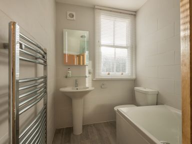 A bathroom with a sink mirror toilet bathtub window and heated towel rail at Kipper Cottage in Port Isaac