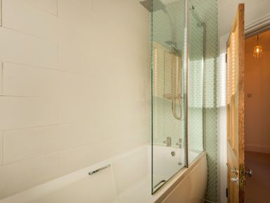 A bathroom with a bathtub shower combination and a wooden door at Kipper Cottage in Port Isaac