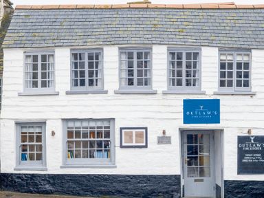 The exterior of a two story white building with gray framed windows and a blue sign reading Outlaw's Fish Kitchen at Kipper Cottage in Port Isaac