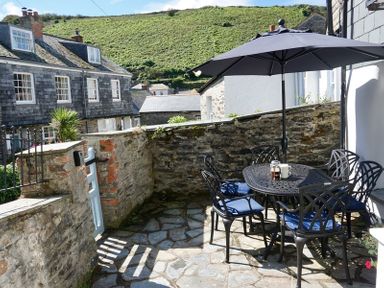 An outdoor patio with a black table and chairs with blue cushions under a large umbrella at Kipper Cottage in Port Isaac