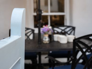 A black metal outdoor dining table with black chairs a vase with flowers and white containers at Kipper Cottage in Port Isaac