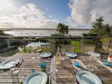 An outdoor dining table set with plates glasses and cutlery overlooking a garden pool and a body of water at Camel Point in Rock