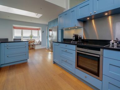 A kitchen with blue cabinets a built in oven wooden floor and a dining area by a window at Camel Point in Rock
