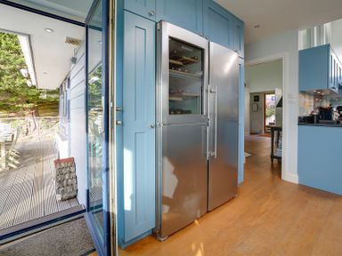 A kitchen with blue cabinets and a stainless steel refrigerator next to a glass door opening to a wooden deck at Camel Point in Rock