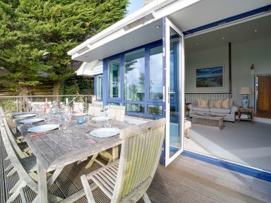 An outdoor wooden dining table with chairs and place settings next to an open door leading to a living room with a sofa and a coffee table at Camel Point in Rock