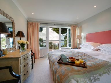 A bedroom with a bed, dresser, two lamps, a tray with breakfast items and a window with a view at Camel Point in Rock