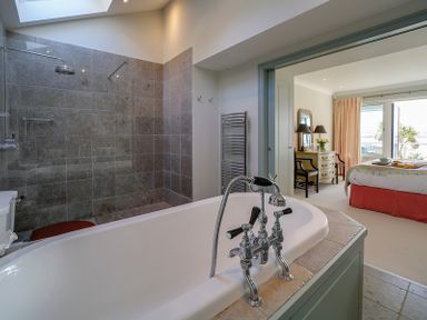 A bathroom with a bathtub shower and toilet opening into a bedroom with a bed chair and dressing table at Camel Point in Rock