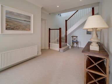 A hallway with carpeted stairs a wooden side table with a lamp and a chair near the staircase at Camel Point in Rock