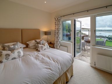 A bedroom with a double bed and patterned pillows and an open door leading to a patio with outdoor furniture and a view of water at Camel Point in Rock