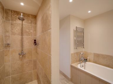 A bathroom with a tiled shower area and a white bathtub with a towel radiator at Camel Point in Rock