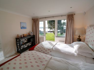 A bedroom with two single beds a lamp a small bookshelf and a view of a garden outside at Camel Point in Rock