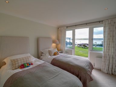 A bedroom with two single beds and a window showing a garden and water view at Camel Point in Rock