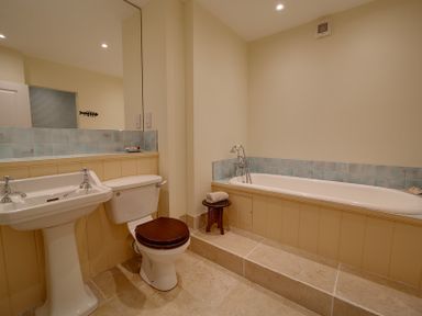 A bathroom with a pedestal sink toilet with wooden seat and a built-in bathtub at Camel Point in Rock