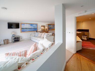 A living room with sofas, a TV on the wall, paintings and a rug next to a bathroom with a red rug at Camel Point in Rock