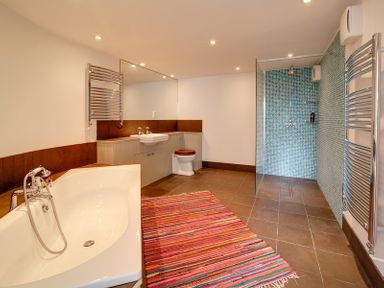 A bathroom with a bathtub a sink a toilet a shower area with blue mosaic tiles and a striped rug on the floor at Camel Point in Rock