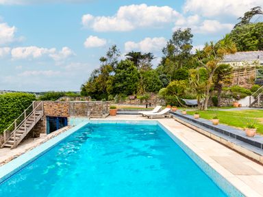 An outdoor swimming pool with two lounge chairs potted plants and trees in a garden at Camel Point in Rock