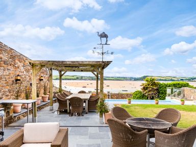 An outdoor patio area with wicker chairs and tables a wooden pergola and plants overlooking a beach and water at Camel Point Rock