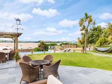An outdoor patio with wicker chairs and table a lawn with palm trees and a hammock overlooking a beach and water at Camel Point in Rock