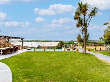 A garden with a lawn a pergola with chairs an infinity pool and sun loungers overlooking a bay at Camel Point in Rock