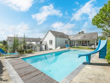 An outdoor swimming pool with a blue slide and lounge chairs near a white house at Landers Field in Rock