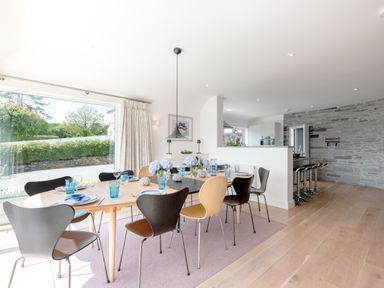 A dining area with a wooden table set with blue glasses and flowers next to a kitchen with bar stools and stone wall at Landers Field in Rock