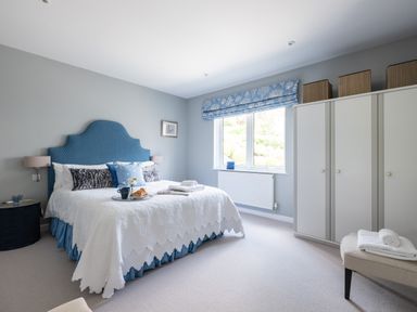 A bedroom with a bed that has a blue headboard white bedspread and blue pillows beside a window with blue blinds and a white wardrobe at Landers Field in Rock
