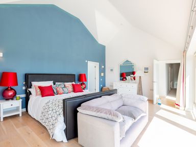 A bedroom with a blue accent wall a bed with red lamps on white nightstands and a gray couch at Landers Field in Rock