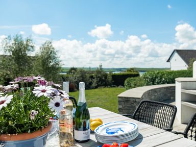 An outdoor table with flowers bottles plates and strawberries with a garden and house in the background at Landers Field in Rock
