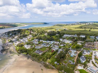 An aerial view of a coastal village with houses fields trees and a sandy beach at Landers Field in Rock