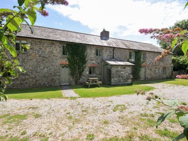 A stone house with a table and bench in the garden at Orchard Cottage in Polzeath