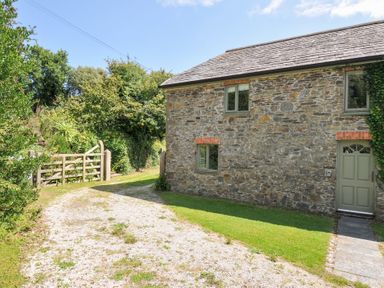 A stone building with windows and a gate at Orchard Cottage in Polzeath