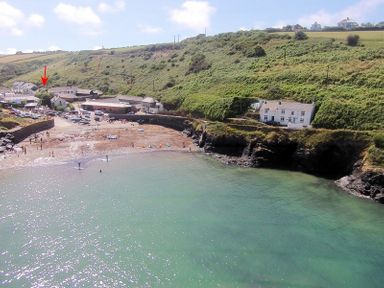 A coastal bay with green hillside and houses overlooking a small beach with boats and people at Stop Tide in Port Isaac