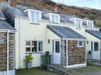 The exterior of a two-story house with cream walls, stone accents, dormer windows, and a railing in front at Stop Tide Port Isaac