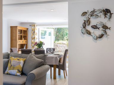 A dining area with a set table and a living room with a sofa and cushions at Stop Tide in Port Isaac