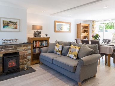 A living room with a gray sofa near a small fireplace and a dining table with chairs at Stop Tide in Port Isaac