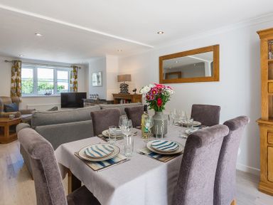 A dining table set with plates glasses and a vase of flowers next to a living room with sofas and a television at Stop Tide in Port Isaac