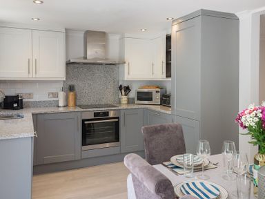 A kitchen with gray and white cabinets a dining table set with plates glasses and a flower vase at Stop Tide in Port Isaac