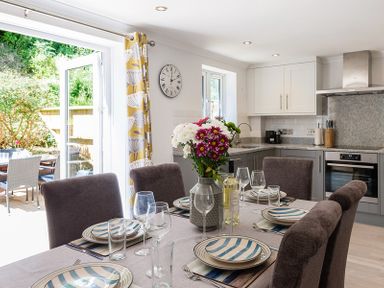 A kitchen and dining area with a table set with plates glasses and flowers at Stop Tide in Port Isaac